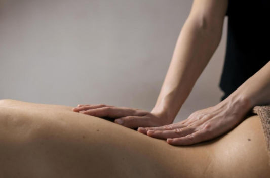 A female massage therapist performing a targeted deep tissue back massage on a client in a serene, neutral-toned studio setting.