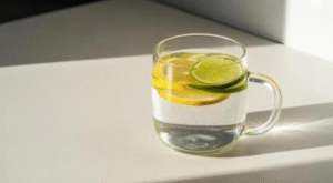 A clear glass mug filled with sparkling water and fresh lemon and lime slices on a bright white table. 